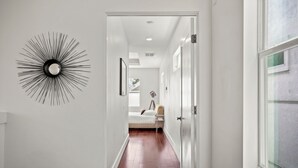 A hallway with a modern sunburst wall decoration, a bed with a white headboard, and a large window on the right. - DwellHTX Modern Designer Home 1 mi frm Downtown 2-Story Getaway w/ Views (Houston)