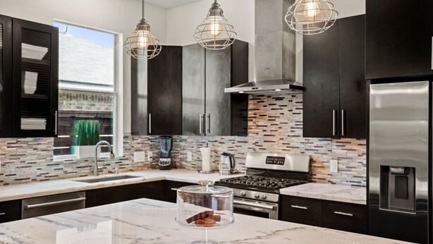 A modern kitchen with dark cabinetry, a tiled backsplash, stainless steel appliances, and pendant lighting. - DwellHTX Modern Designer Home 1 mi frm Downtown 2-Story Getaway w/ Views (Houston)