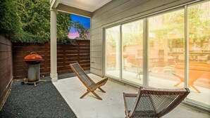 A patio with a grill, a chair, and a view of the backyard through large windows. - DwellHTX Modern Designer Home 1 mi frm Downtown 2-Story Getaway w/ Views (Houston)