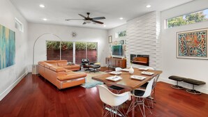 A modern living room with a brown leather sofa, a dining table with chairs, a TV, and a fireplace. - DwellHTX Modern Designer Home 1 mi frm Downtown 2-Story Getaway w/ Views (Houston)