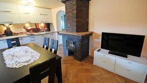 Una cocina moderna con chimenea de ladrillo, un comedor con mesa y sillas, y un televisor sobre un mueble blanco.
