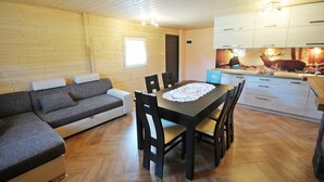 Una habitación acogedora con techo de madera, un sofá, una mesa de comedor con sillas y una zona de cocina con armarios y una decoración de ciervo en la pared.
