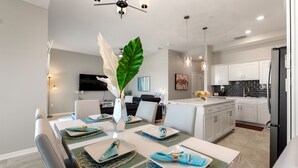 A modern kitchen with white cabinets, a black refrigerator, and a dining area with a table set for four. - Fireworks from Balcony, No Resort Fees! (Kissimmee)