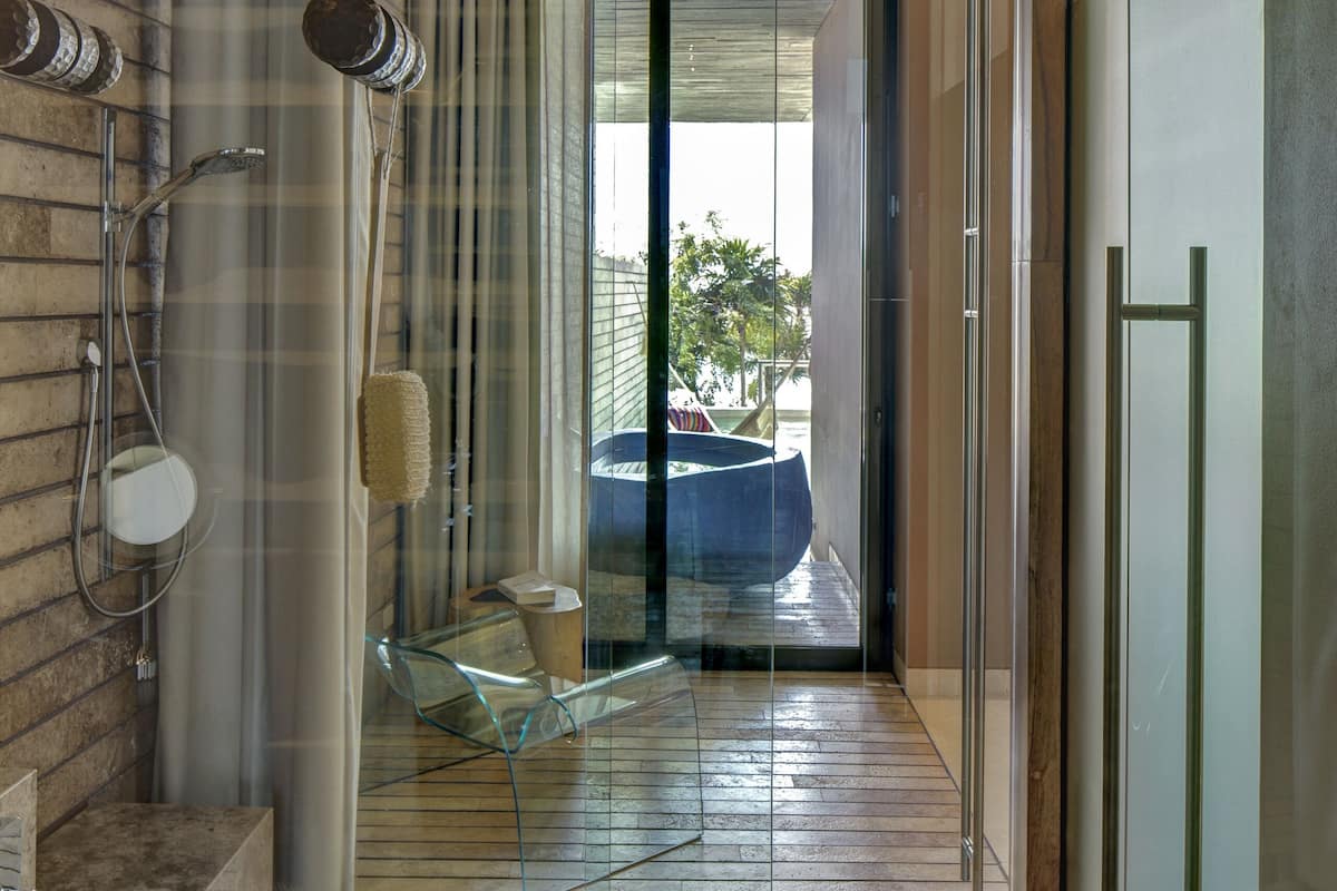 A modern bathroom with a glass shower enclosure, wooden flooring, and a view of the outdoors.