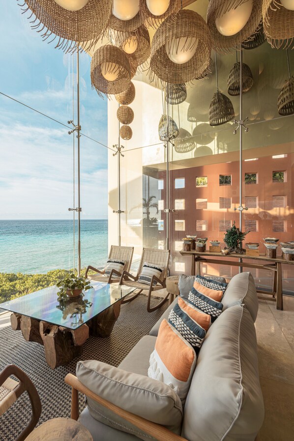 Un salón moderno con una mesa de vidrio, lámparas colgantes de mimbre y vista al océano.