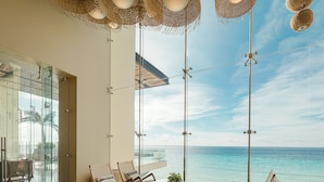 A modern living room with a large sofa, wooden chairs, and a glass table. It features a view of the ocean and a clear sky. - La Casa de la Playa by Xcaret-All Inclusive, Adults Only (Playa del Carmen)
