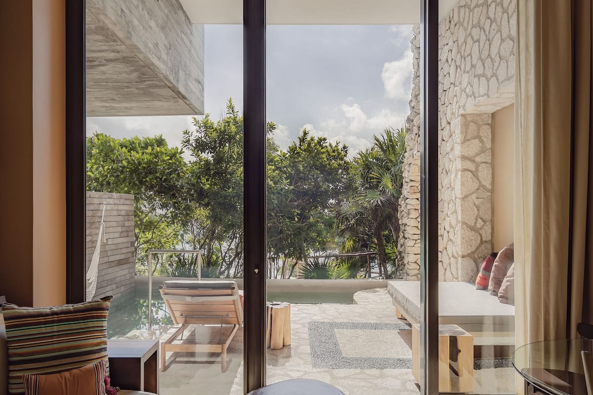 A modern living room with a large sliding glass door leading to a patio with outdoor furniture and a view of greenery.
