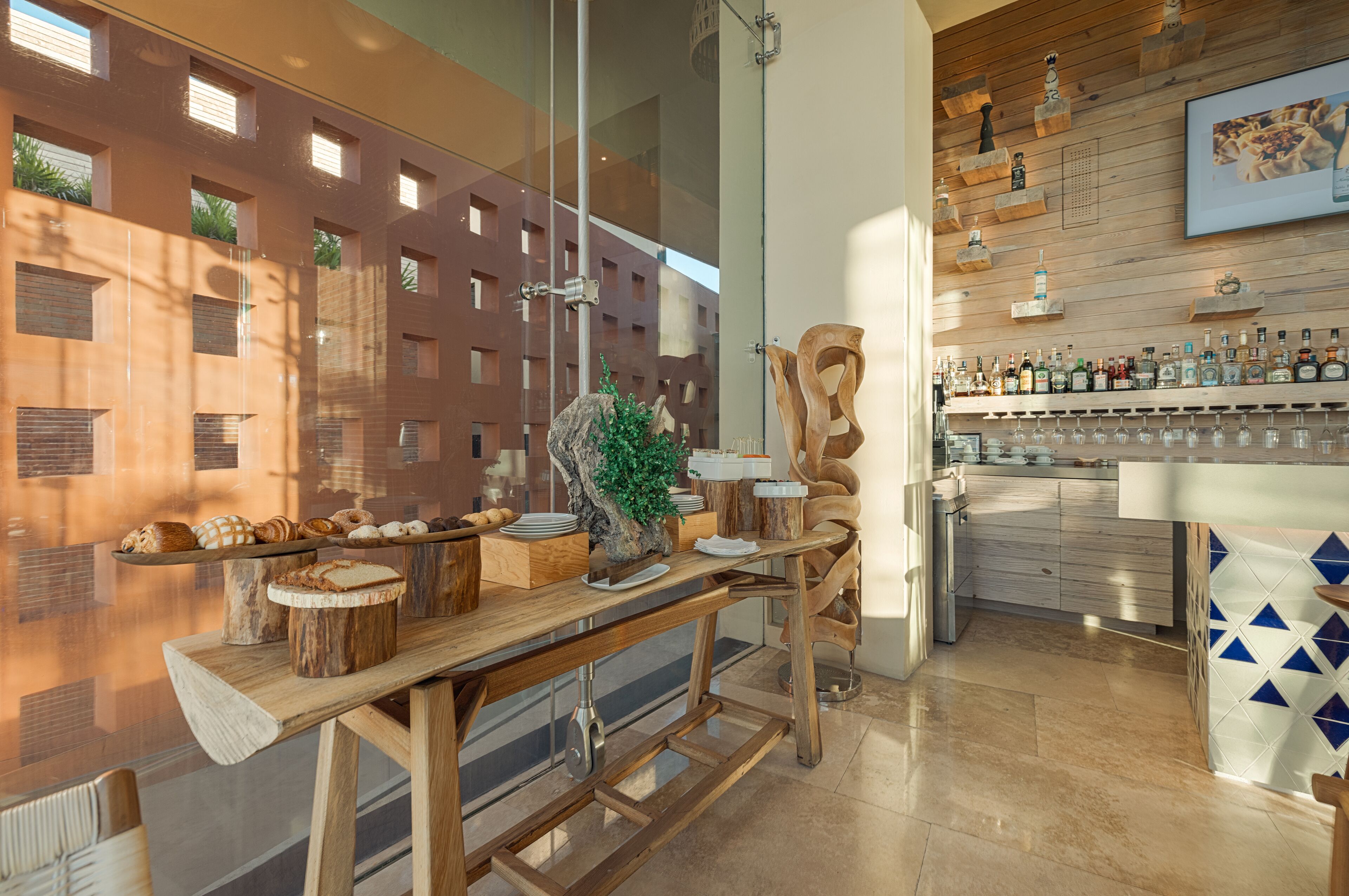 Una cocina moderna con encimeras de madera, una zona de bar con botellas y vistas a un edificio con amplios ventanales.
