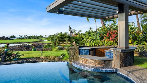 A pool with a stone and tile edge, a wooden deck, and a view of a golf course and tropical vegetation. - 🏖️Mauna Lani 4BR Home w/ Private Pool + Central AC (Kamuela)