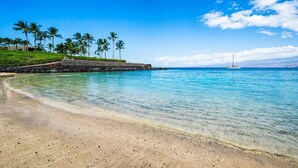 A beach with clear turquoise water, a sandy shore, and a small sailboat in the distance. - 🏖️Mauna Lani 4BR Home w/ Private Pool + Central AC (Kamuela)