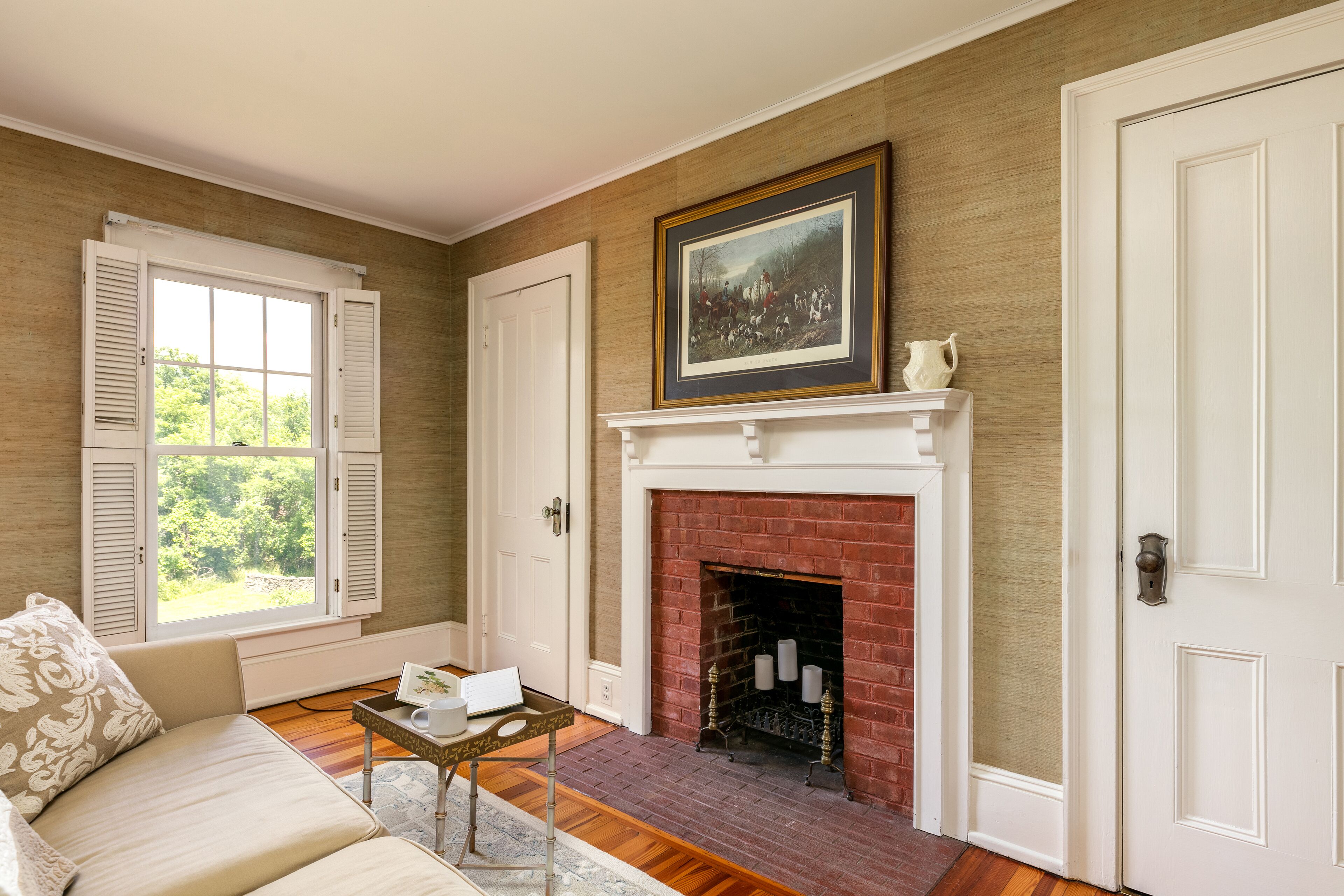 A room with a fireplace, a sofa, a table with a cup and a book, and a framed picture above the fireplace.
