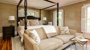 Een hemelbed met een beige gestoffeerde bank, een tafeltje met kop en schotel, en een nachtkastje met lampen.