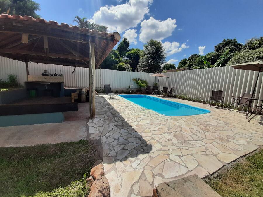 A backyard with a swimming pool, stone patio, covered seating area, and a fenced garden.