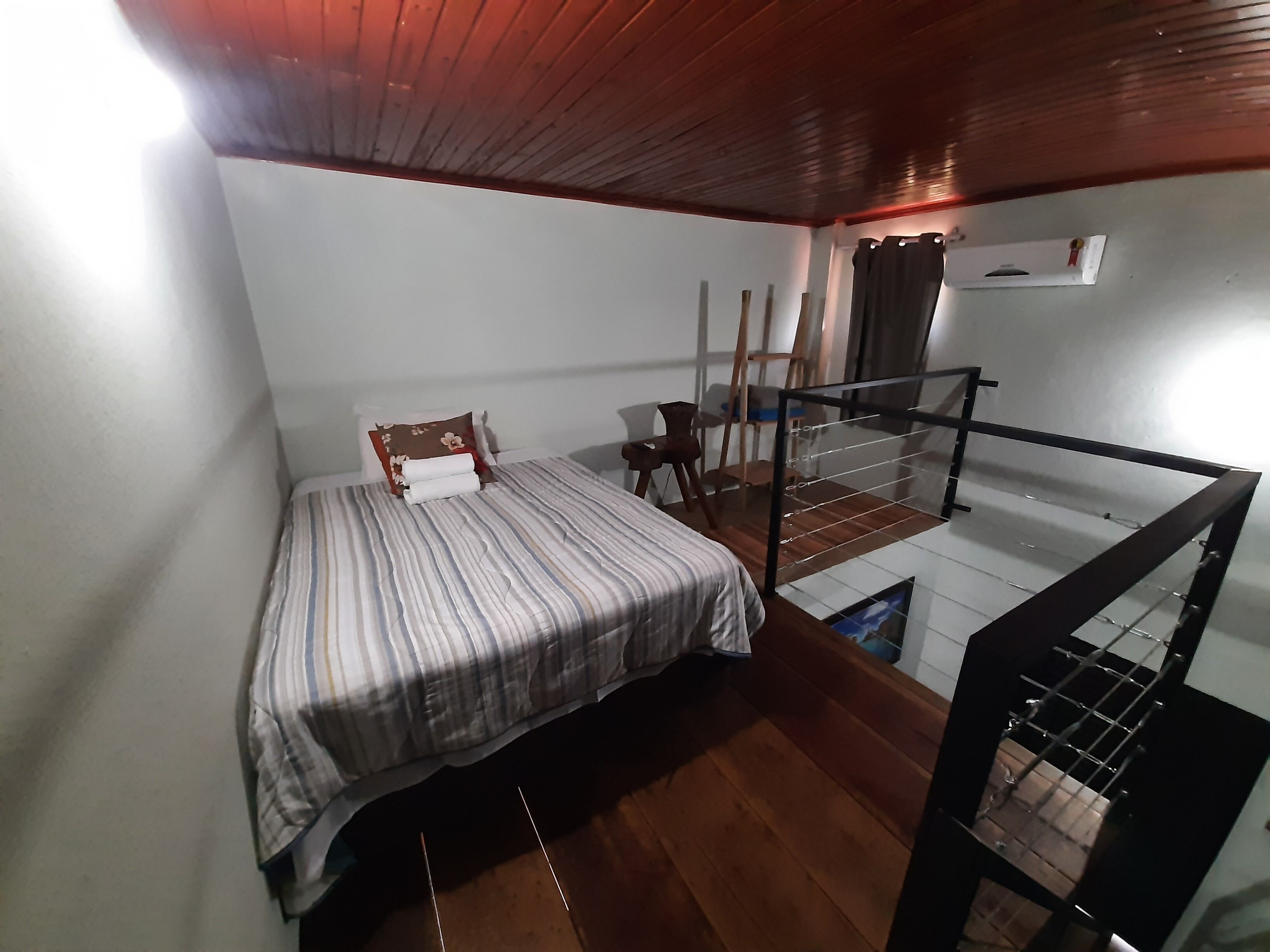 Ein Zimmer mit einem Bett, Holzboden, einem kleinen Tisch, einem Stuhl und einem Glasgeländer.