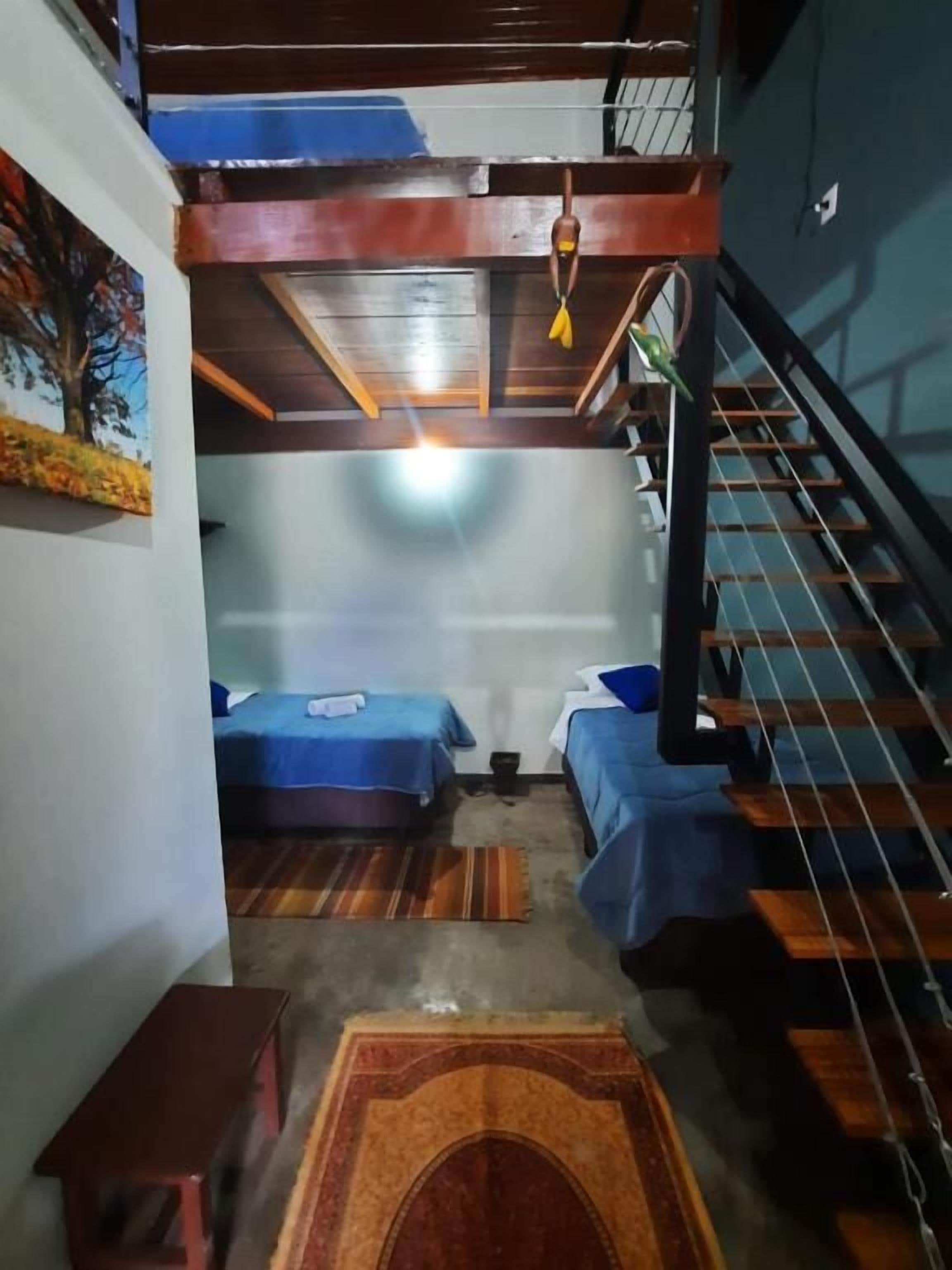 A room with two beds, a wooden bench, a staircase, and a painting on the wall.