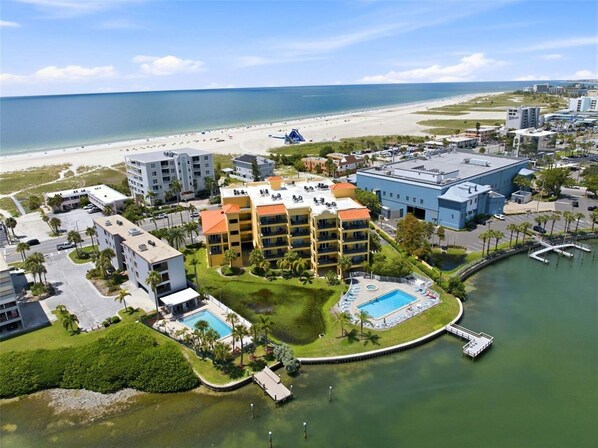 A coastal hotel with multiple buildings, a swimming pool, and a beach in the background.