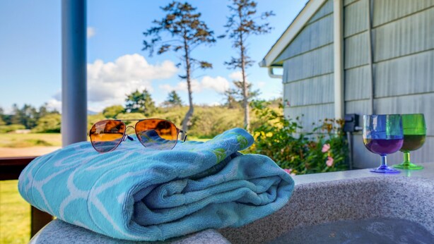 A towel, sunglasses, and two wine glasses on a balcony with a view of trees and a building.