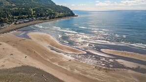 A coastal beach with a forested hillside, sandy shore, and clear blue water.