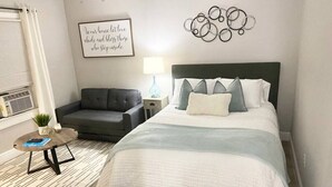 Une chambre à coucher avec un lit, un canapé gris, une petite table ronde et un mur orné d’un motif circulaire.