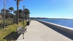 Une promenade en bord de mer agrémentée de bancs, de palmiers et offrant une vue dégagée sur l’océan.