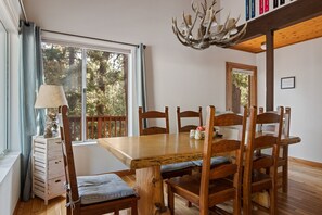 Ein Essbereich mit einem Holztisch, Stühlen, einer Chandelüster und Blick auf Bäume durch ein großes Fenster.