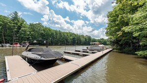 A dock with a boat and a covered area, surrounded by trees and calm water. - Cozy Chalet w/ Lake Access & Game Room (Oakland)