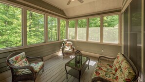 A sunroom with wicker furniture, large windows, and a ceiling fan. - Cozy Chalet w/ Lake Access & Game Room (Oakland)