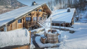 Un chalet en bois avec un toit en pente, une terrasse en bois et un jacuzzi installé dans la neige.