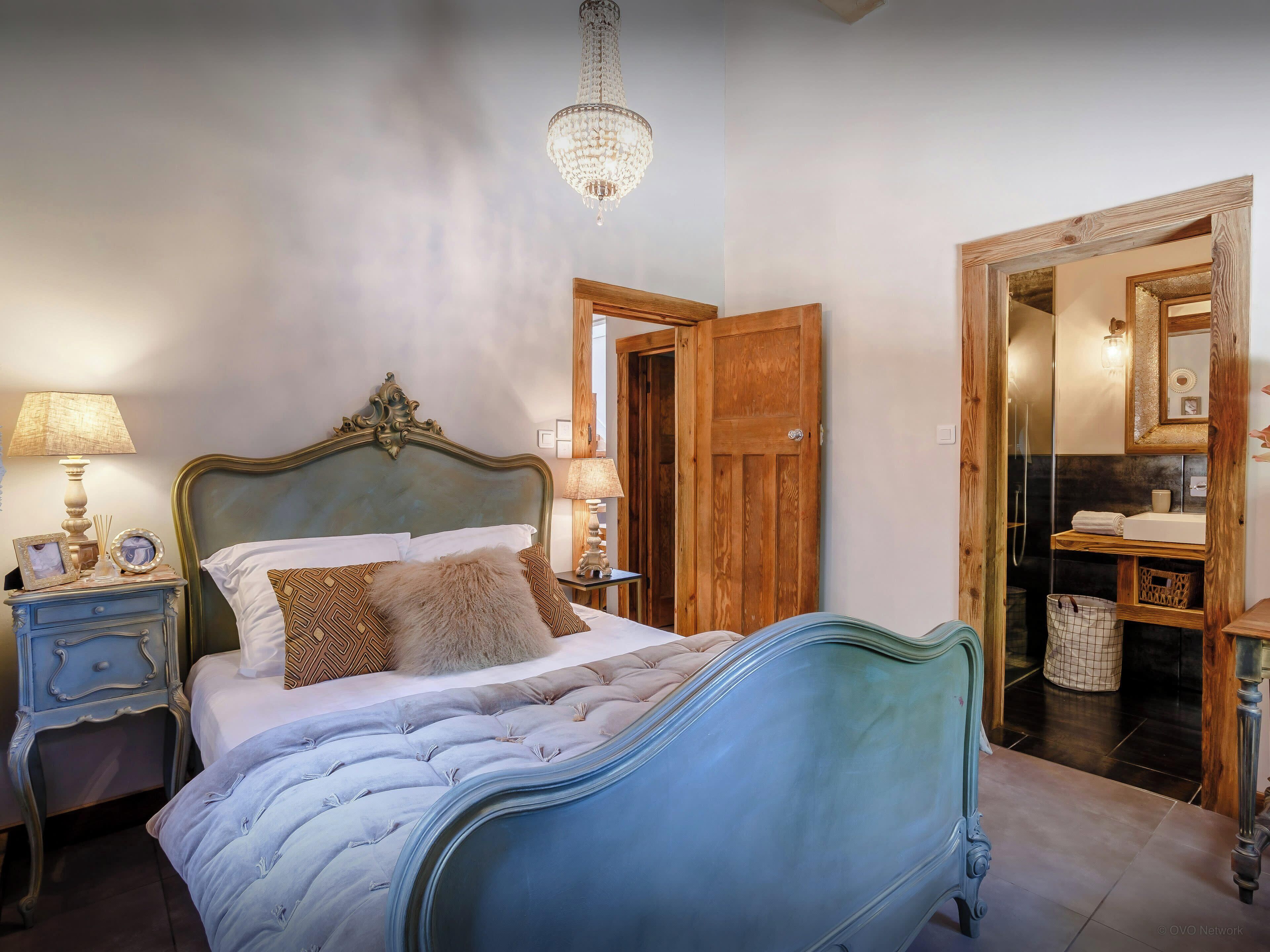 Een slaapkamer met een groot bed, een houten deur, een badkamer met een spiegel en een kroonluchter.