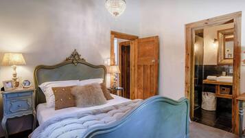 Een slaapkamer met een groot bed, een houten deur, een badkamer met een spiegel en een kroonluchter.