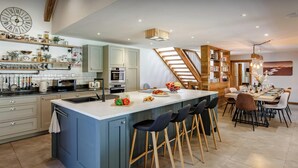 Une cuisine moderne dotée d’un îlot central, de tabourets de bar et d’un coin repas avec un escalier en bois.