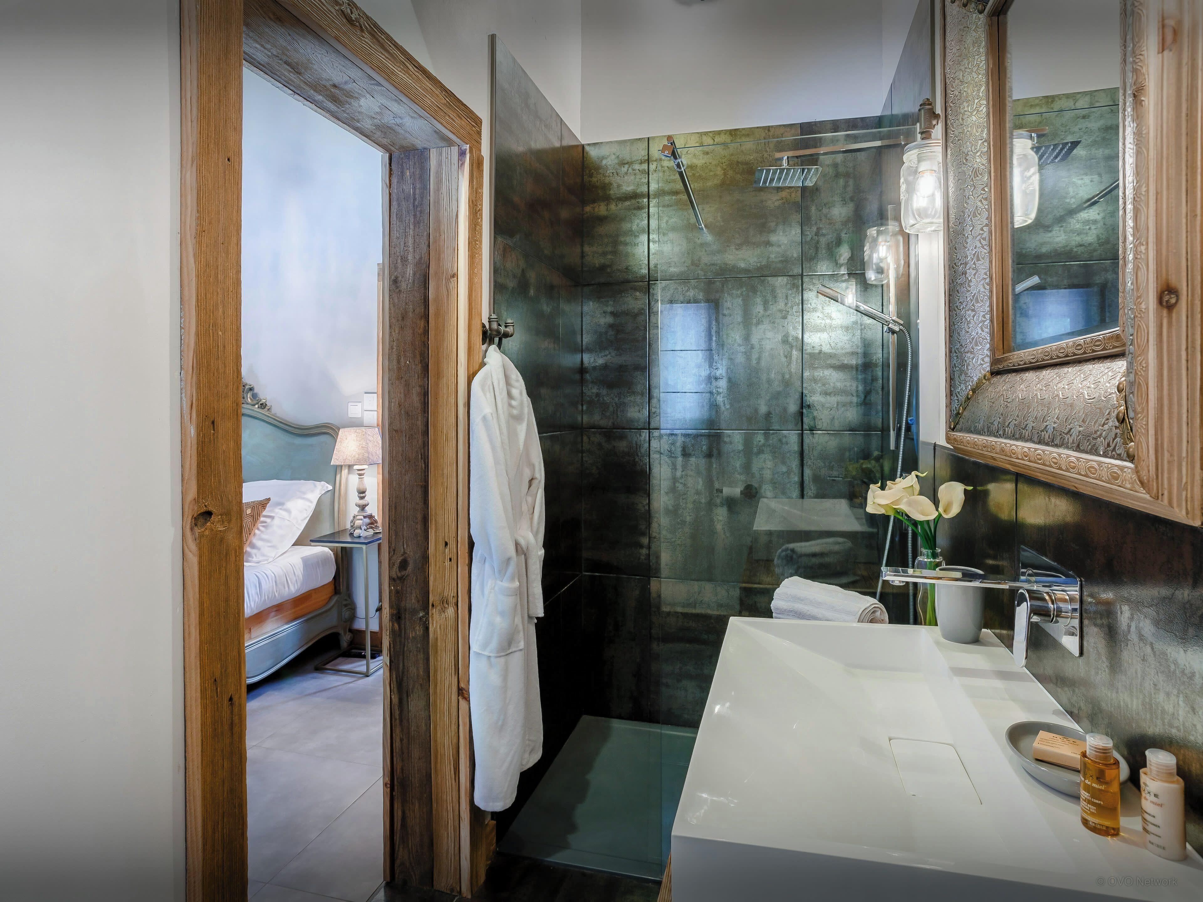 Une salle de bain moderne avec une douche à parois de verre, un lavabo blanc agrémenté d’articles de toilette et un miroir encadré en bois.