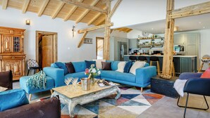 Un salon spacieux avec un canapé bleu, un meuble en bois et une cuisine à l’arrière-plan.