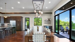 Una cocina moderna con una larga mesa de comedor, suelo de madera y ventanas amplias que ofrecen vistas al exterior.