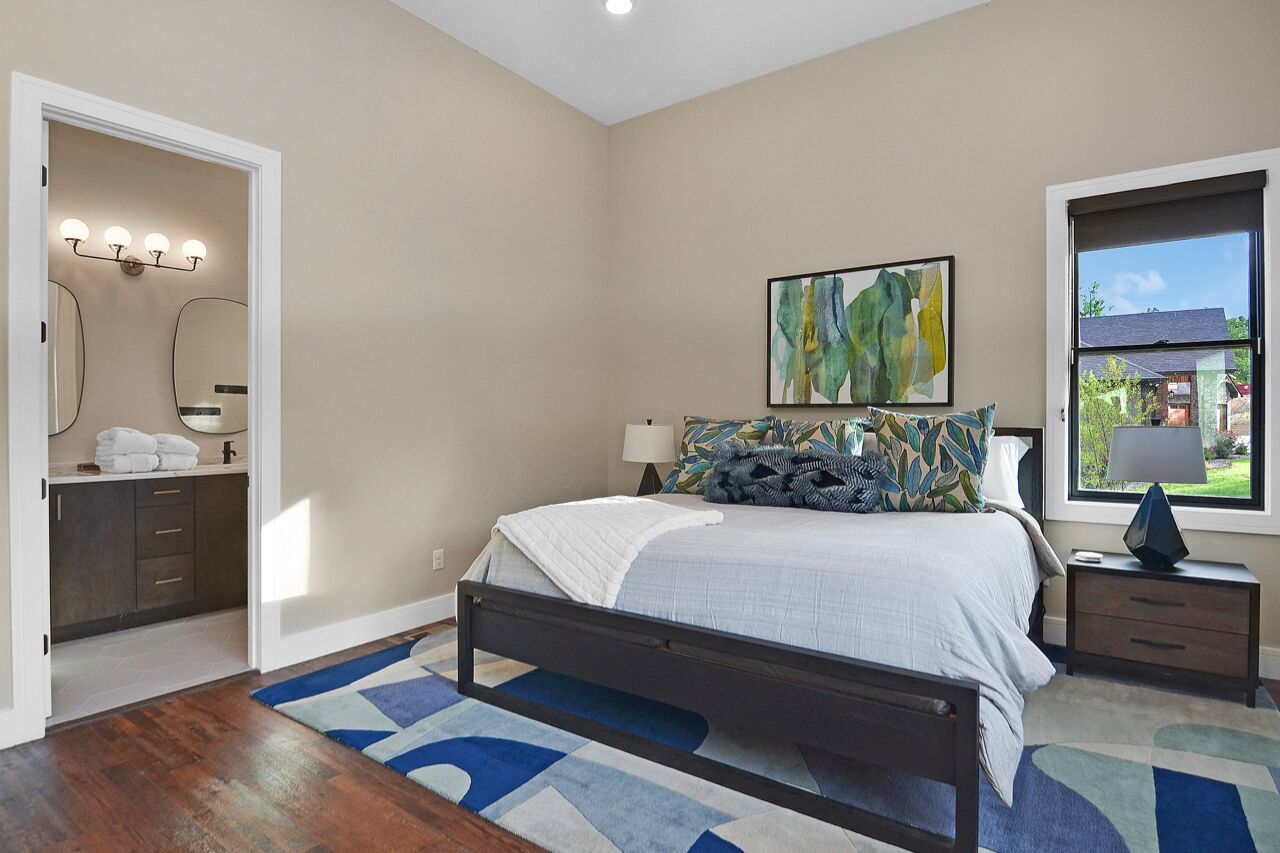 A bedroom with a bed, bedside tables, a window with a view, and a bathroom with a vanity and mirror.