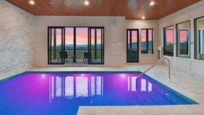Una piscina interior moderna con vista a la puesta de sol sobre montañas.