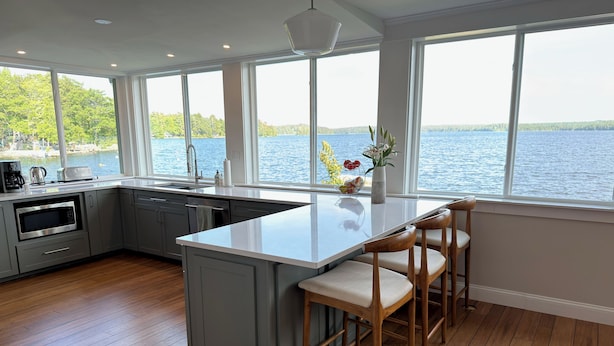 A modern kitchen with a large island, bar stools, and a view of a lake.