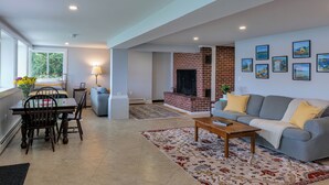 A spacious living room with a fireplace, a dining area, and a sofa with cushions. - Lakefront for 15, private beach and dock (Dedham)