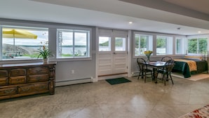 A spacious room with a dining area, a bed, and large windows offering a view of the outdoors.