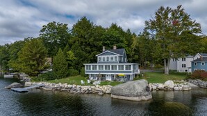A two-story house with a dock extending into a lake, surrounded by trees.