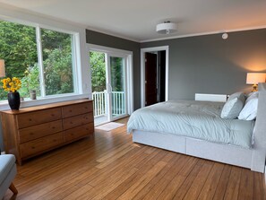 A bedroom with a large bed, a dresser, and a window with a view of greenery.