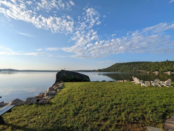 Vista para o lago com área gramada, formação rochosa e cadeiras Adirondack.