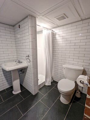 A bathroom with white subway tiles, a white pedestal sink, a toilet, and a shower with a white curtain.