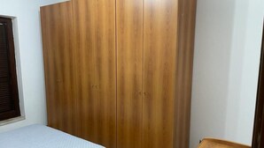 Un dormitorio con un armario de madera, una cama con colcha blanca y una mesita de noche de madera.