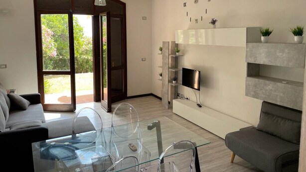 Una sala de estar moderna con una mesa de centro de vidrio, un sofá gris y un televisor montado en la pared.