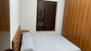 Une chambre à coucher avec un lit, une fenêtre avec des stores et une armoire en bois.