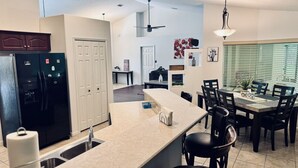 Une cuisine moderne dotée d’un îlot central, d’un coin repas avec une table et des chaises, et d’un ventilateur de plafond.