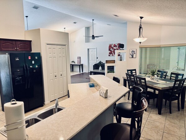 A modern kitchen with a central island, a dining area with a table and chairs, and a ceiling fan.