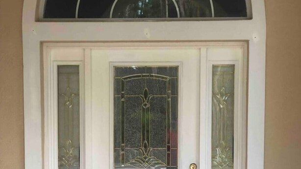 Une porte d’entrée blanche avec un panneau de verre et une grille décorative en métal.