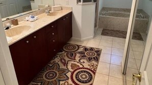 Une salle de bain dotée d’un meuble-lavabo à deux vasques, d’un grand miroir avec éclairage intégré, d’une douche avec une porte en verre et d’un tapis à motifs.